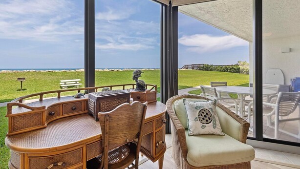 A modern outdoor seating area with a view of the ocean, a wicker table, and a cushioned chair. - Chadham by the Sea 118 (New Smyrna Beach)