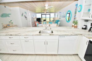 A kitchen with white cabinets, a marble countertop, and a dishwasher. - Chadham by the Sea 119 (New Smyrna Beach)