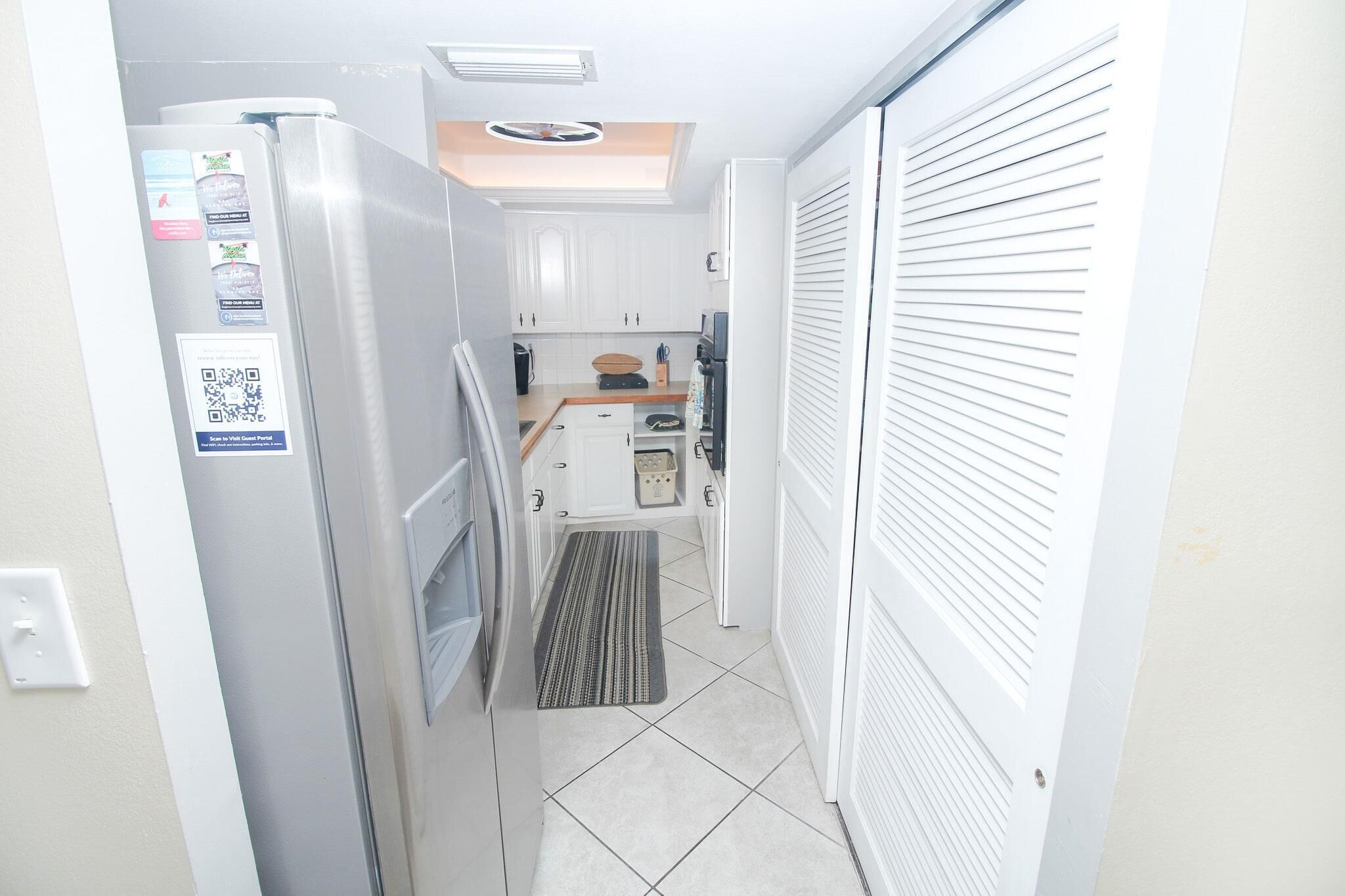 A narrow kitchen with white cabinets, a built-in oven, and a microwave. There is a small countertop with a coffee maker and a kettle.
