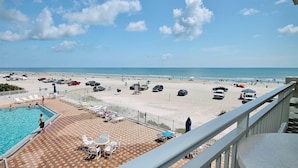 Blick auf einen Strand vom Balkon aus, mit Pool, Liegestühlen und Sonnenschirmen.