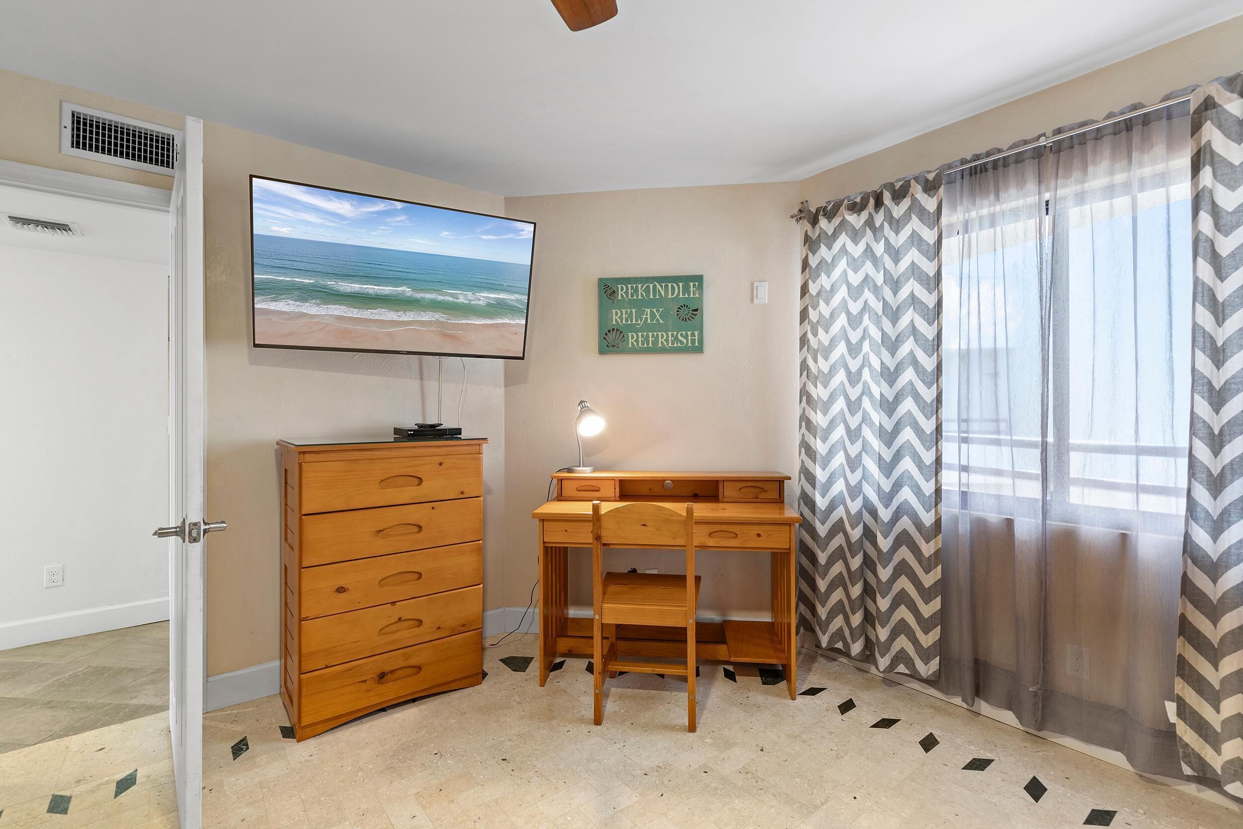 Un dormitorio con cómoda de madera, escritorio, televisor y ventana con cortinas.