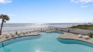 Ein Pool mit gewölbter Kante, umgeben von Liegestühlen und einer Palme, mit Blick auf einen Strand.