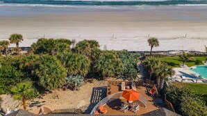 Blick auf einen Strand mit Poolbereich, Palmen und blauem Himmel.