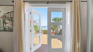 Ein Zimmer mit einer Tür, die auf einen Balkon mit Blick auf den Strand und Palmen führt.