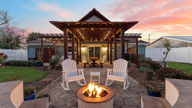 Un patio con un pozo de fuego, dos sillas Adirondack blancas y una pérgola con luces colgantes.