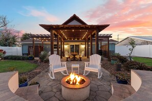 A patio area with a fire pit, two white Adirondack chairs, and a pergola with string lights. - Smyrna Dreams (New Smyrna Beach)