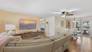 Una sala de estar con sofá color beige, televisor y ventilador de techo.