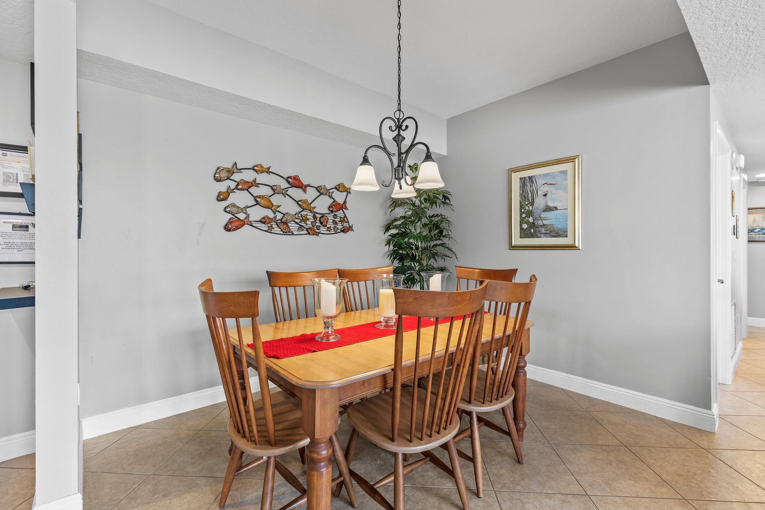 A dining area with a wooden table, six chairs, a red runner, a chandelier, a wall art piece, and a framed picture.