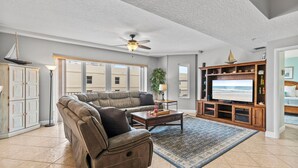 A spacious living room with a large sectional sofa, a flat-screen TV, and a ceiling fan. - Sanibel 601 (Daytona Beach Shores)