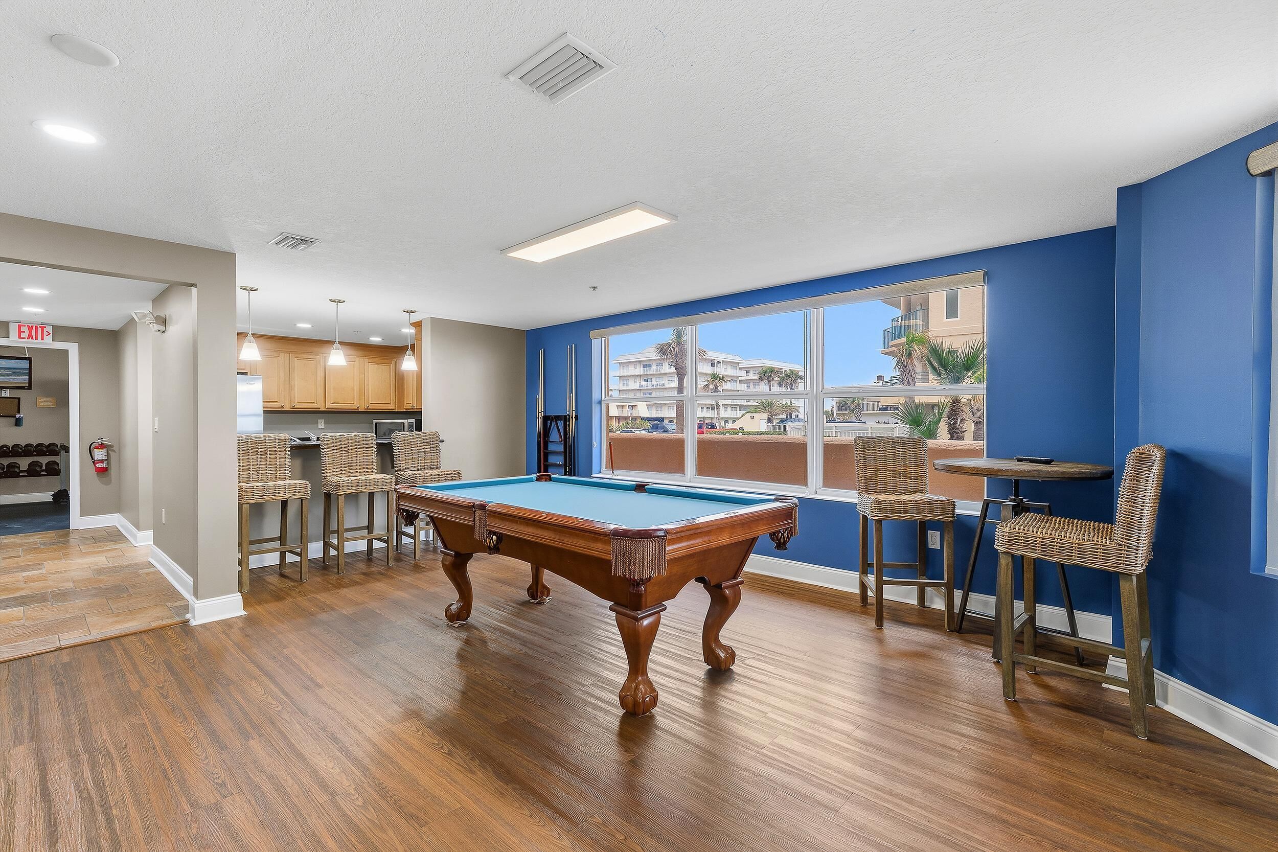 A pool table in a room with a view, wooden flooring, and a bar area with wicker chairs.