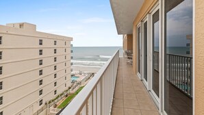 A balcony with a view of the ocean, a pool area, and adjacent buildings. - Sanibel 601 (Daytona Beach Shores)