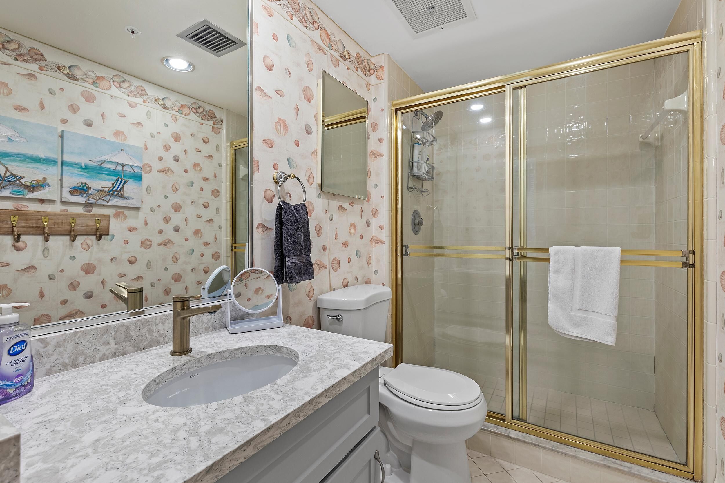 A bathroom with a marble sink, a toilet, a glass-enclosed shower, and a wall with a seashell pattern.