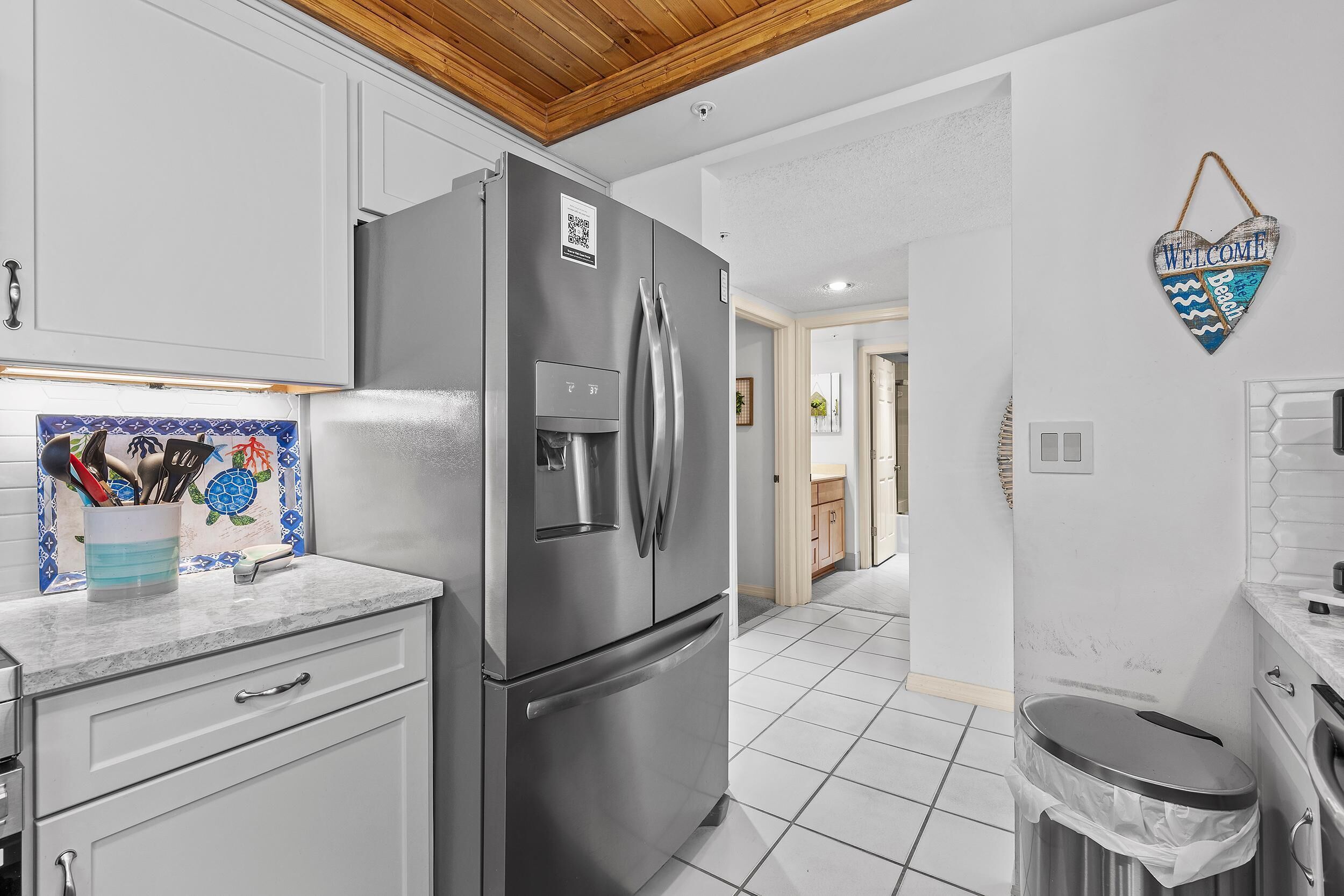 A modern kitchen with a stainless steel refrigerator, white cabinets, and a tiled floor.
