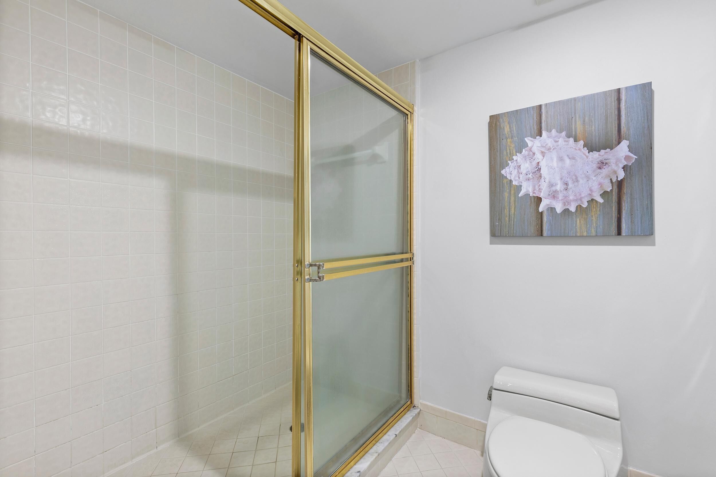 Un baño con mampara de vidrio, azulejos blancos y un inodoro.