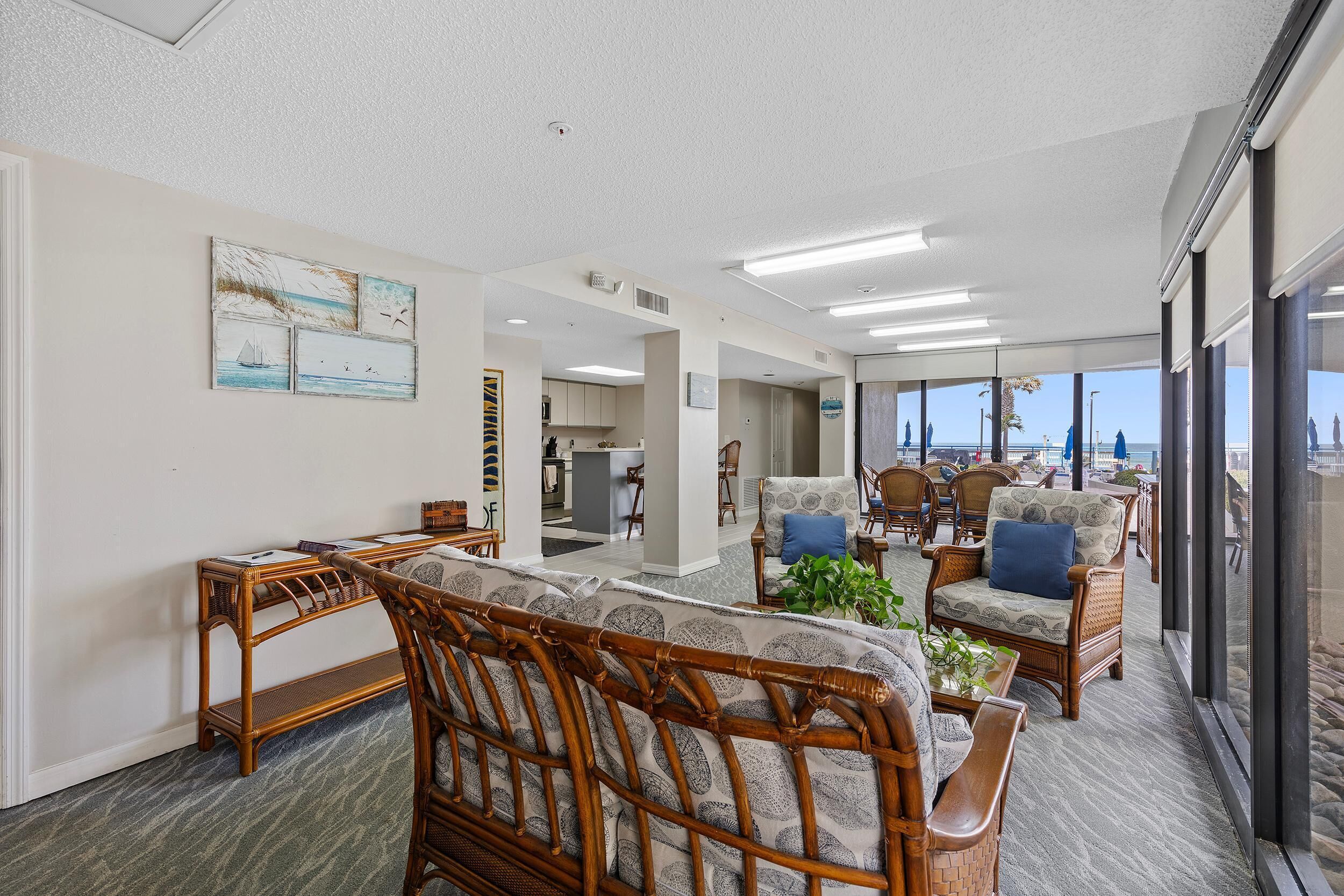 A spacious living area with wicker furniture, a view to the outside, and a kitchen in the background.