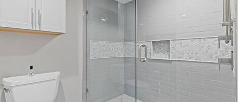 Une salle de bain moderne dotée d’une douche à parois de verre, de toilettes et d’un lavabo.