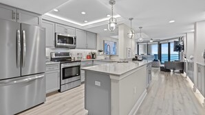 A modern kitchen with stainless steel appliances, a central island, and pendant lighting. - Ebb Tide 505 (New Smyrna Beach)
