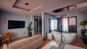 Ett modernt hotellrum med en stor säng, en soffa, en TV, en växt och ett badrum med badkar.