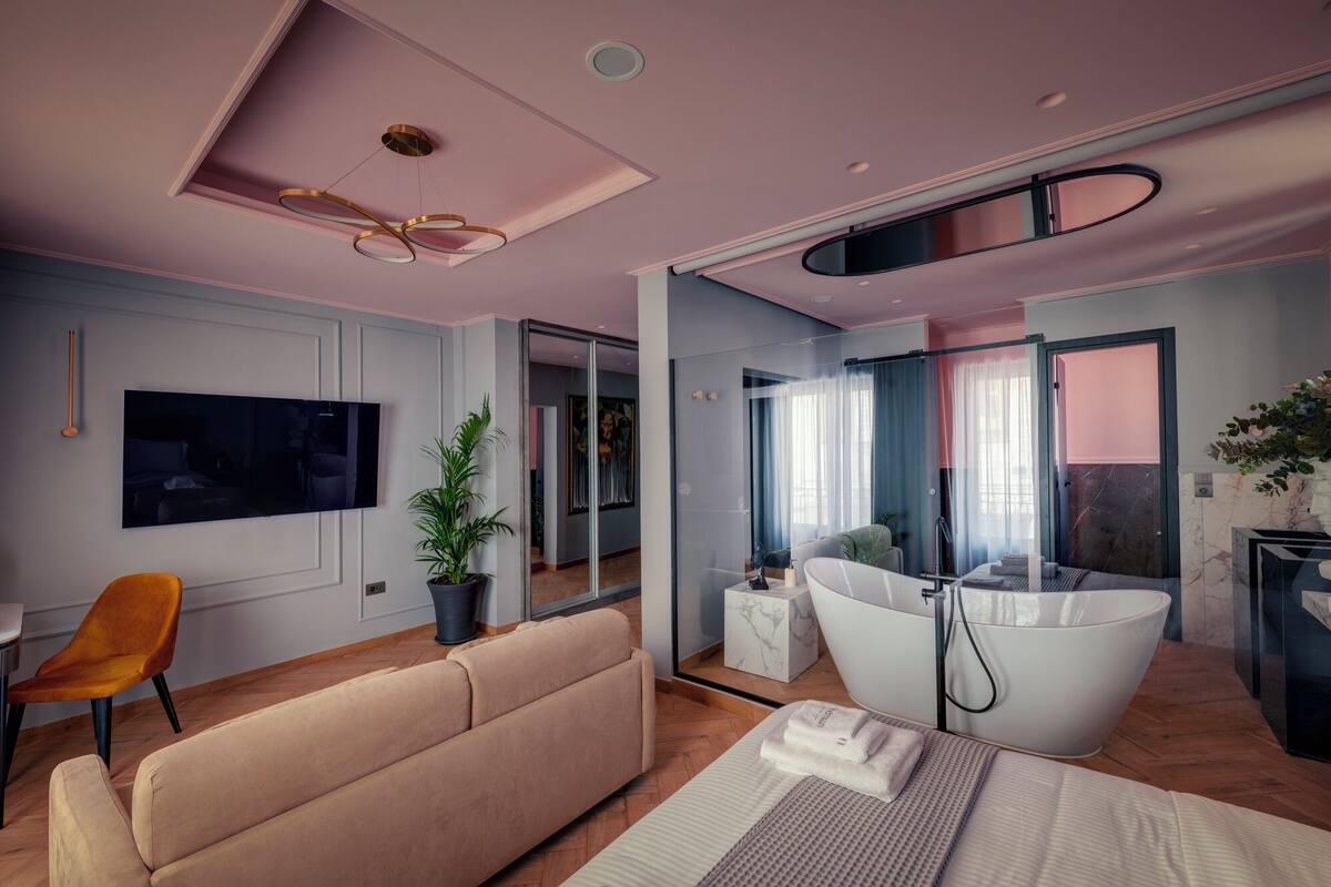 Una habitación de hotel moderna con una cama grande, un sofá, un televisor, una planta y un baño con bañera.