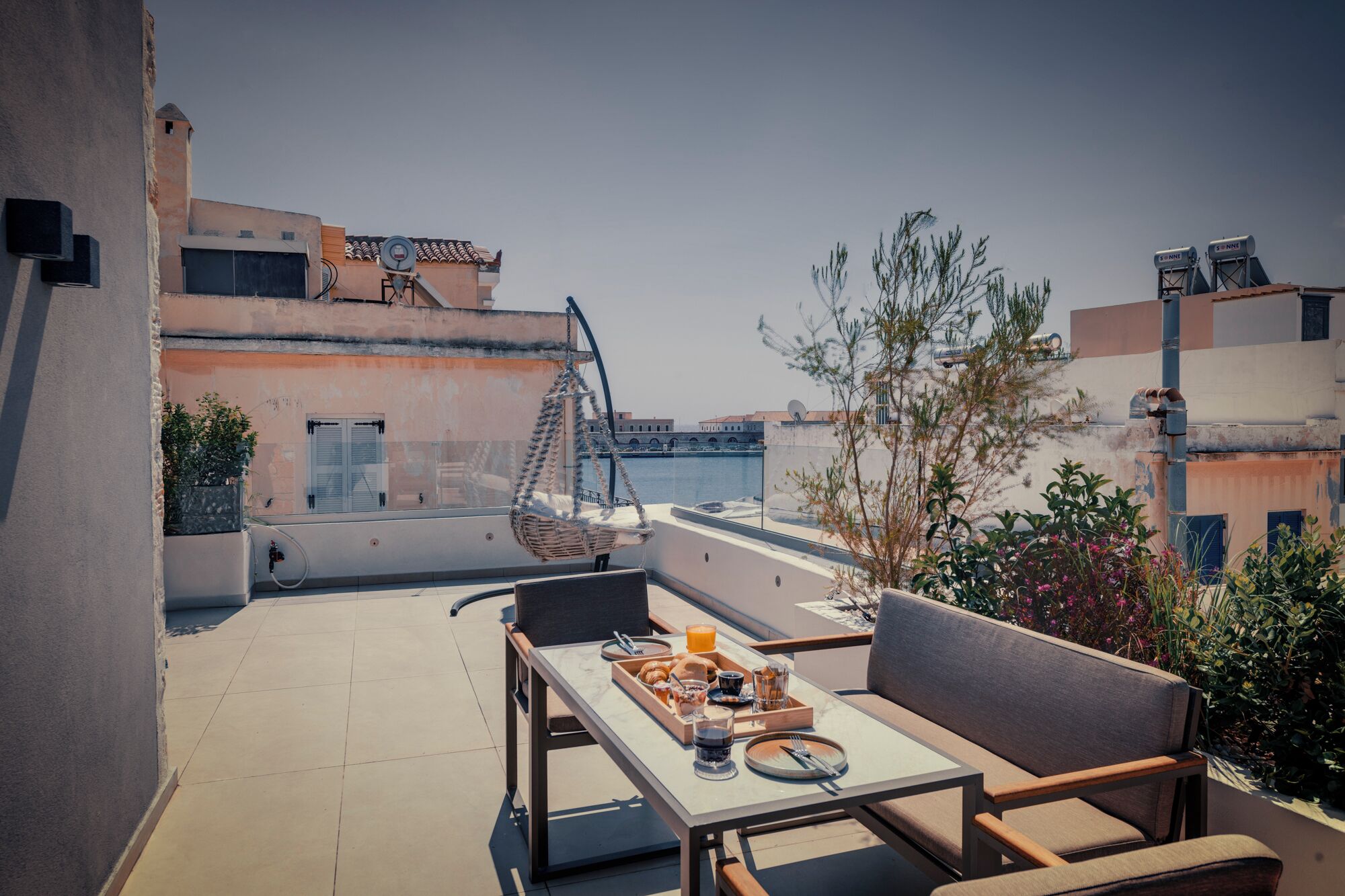 A balcony with a table set for breakfast, overlooking a cityscape with buildings and a bridge.