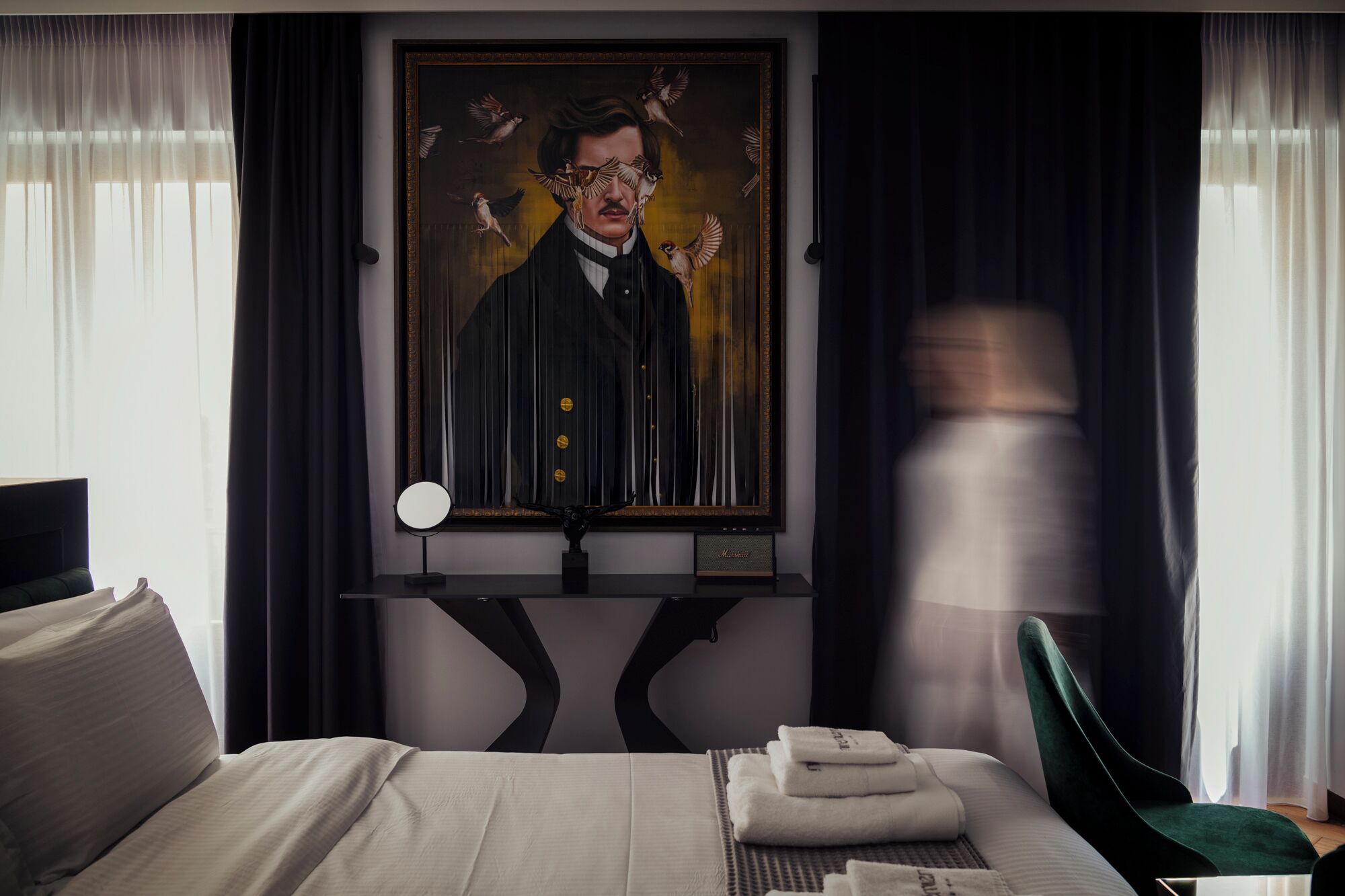 Habitación de hotel con una cama, una obra de arte grande enmarcada en la pared, una mesita de noche con lámpara y una silla.
