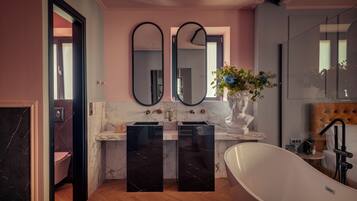 Un baño moderno con una bañera independiente, encimeras de mármol, dos espejos grandes y un jarrón con flores.