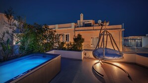 En takterrass med ett bubbelbad, en hängstol och utsikt över en byggnad med en skorsten.