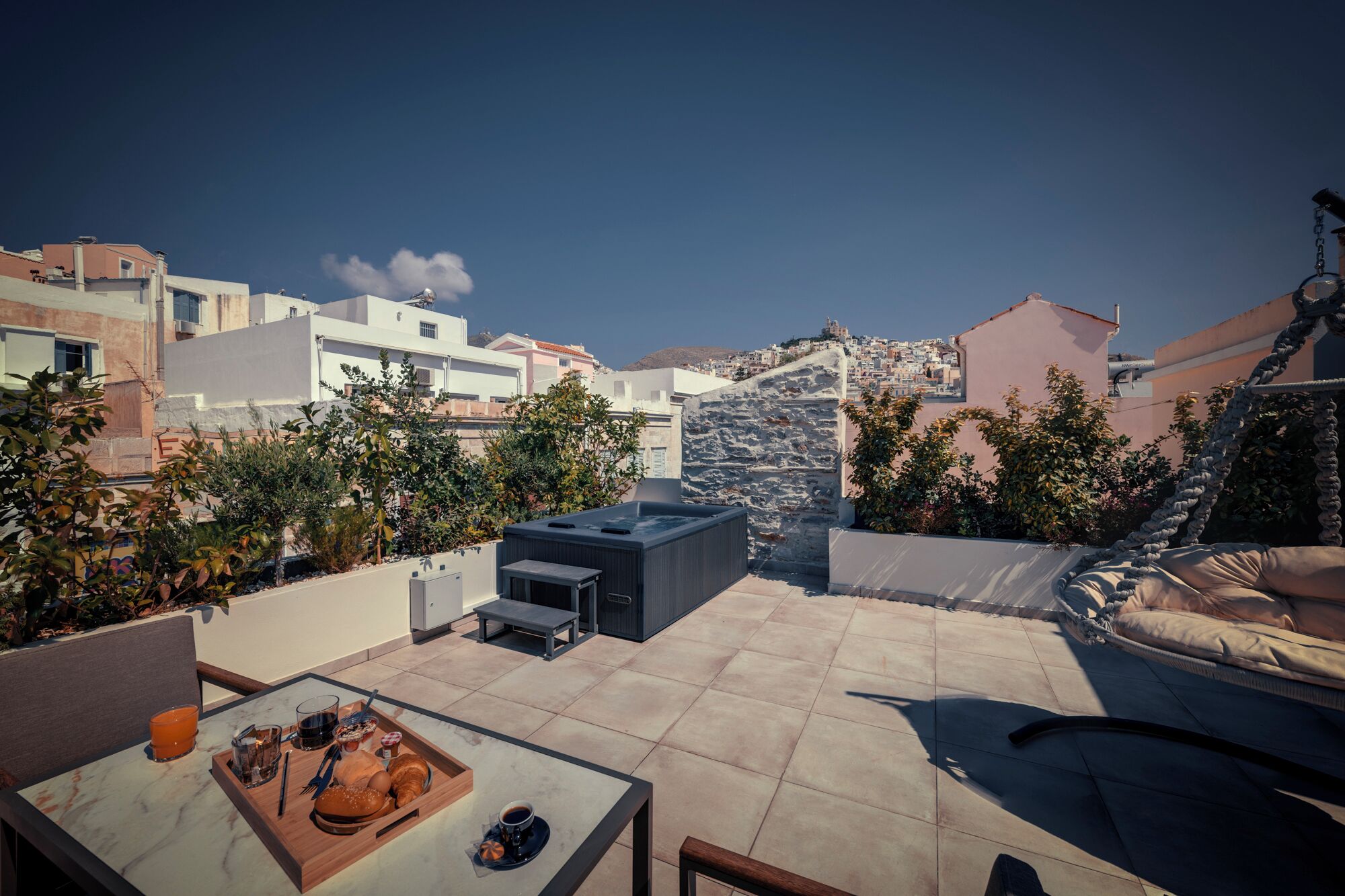 Una terraza en la azotea con una mesa para dos, un muro de piedra y vistas a un pueblo en la ladera.