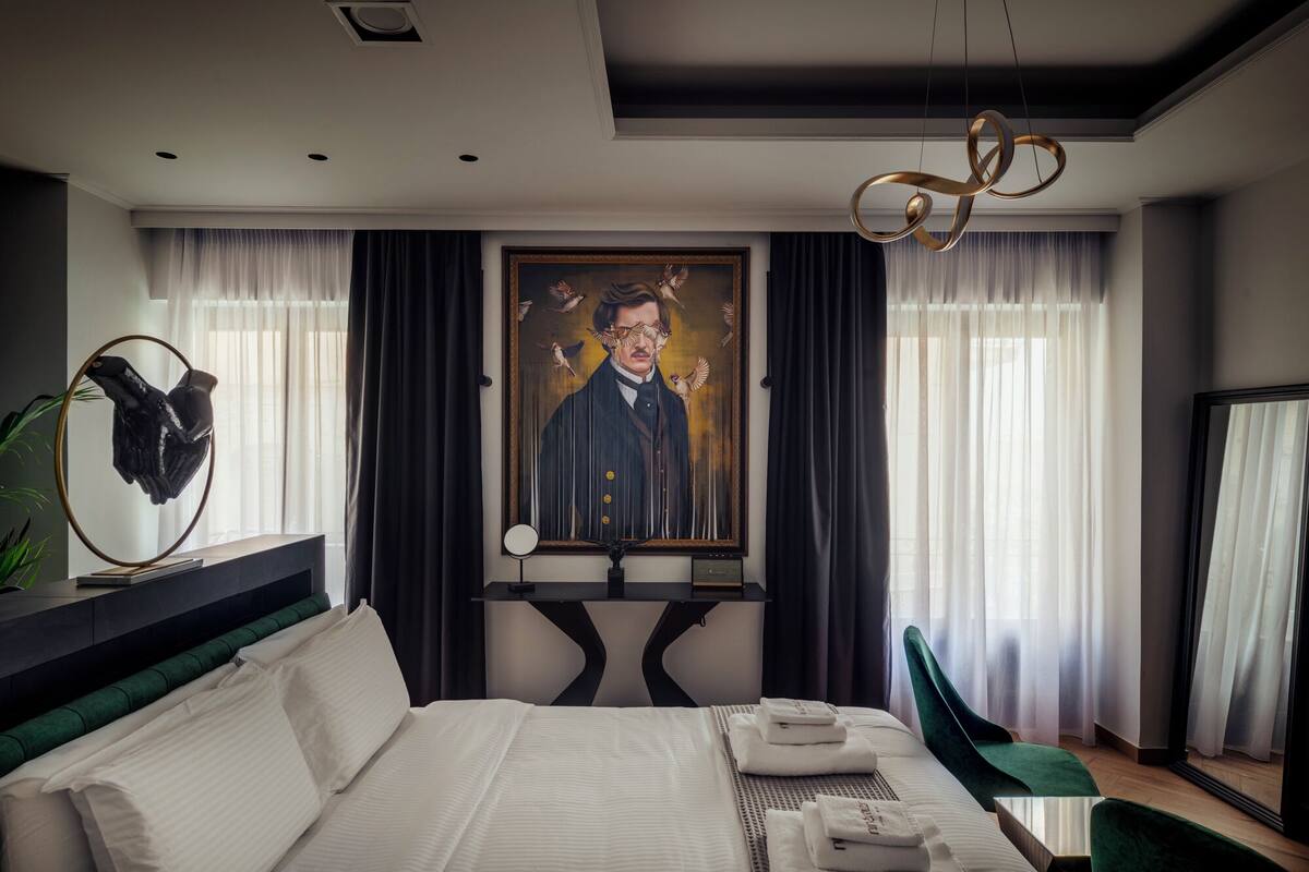Una habitación de hotel moderna con una cama grande, un cuadro en la pared y una lámpara de techo original.