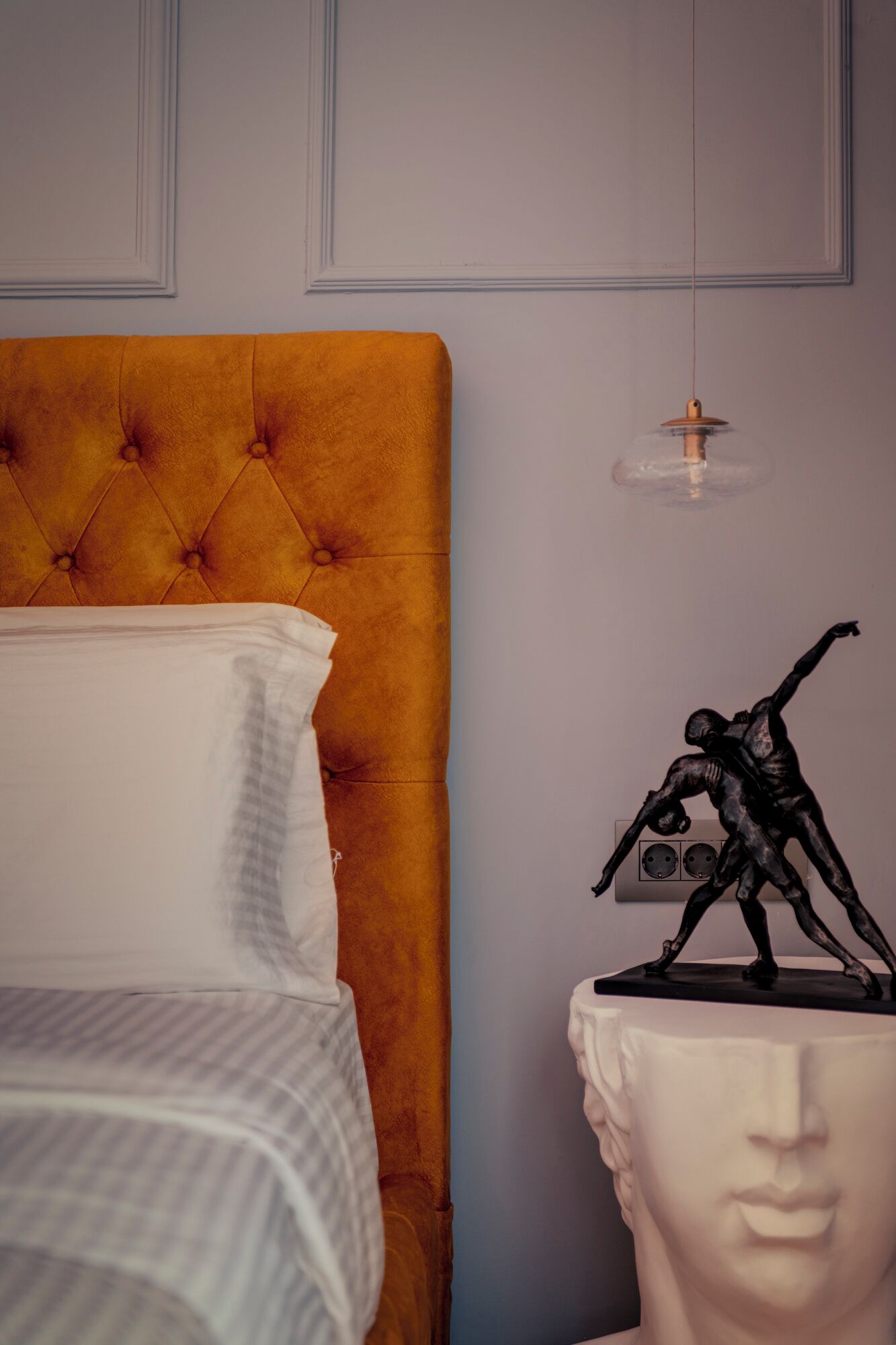 Ein Bett mit einem gebügelten Kopfteil, einem weißen Kopfkissen und einem weißen Nachttisch mit einer Skulptur.