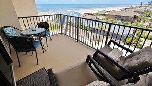 A balcony with a view of the beach, a table with chairs, and a sofa.