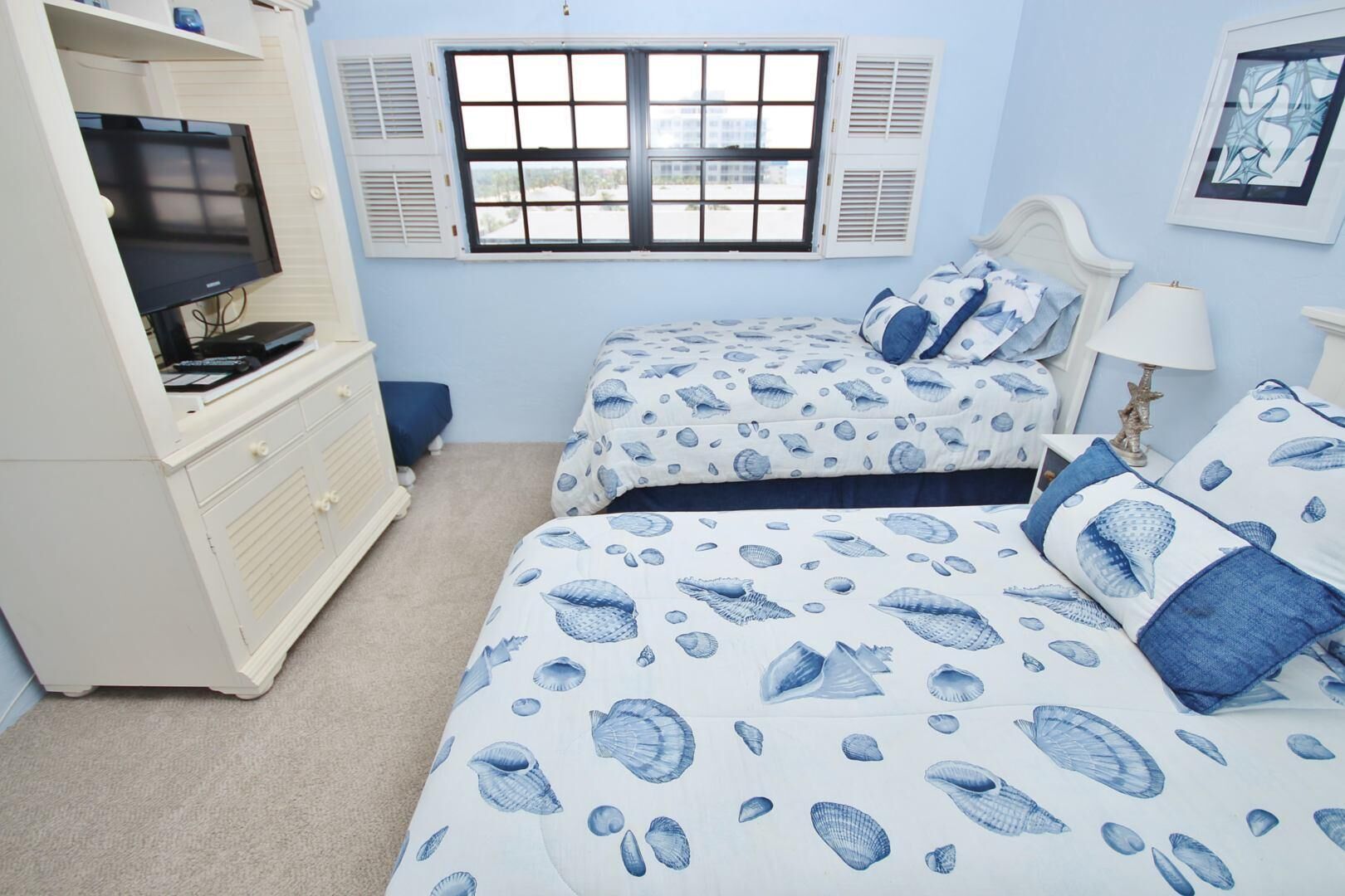 Een slaapkamer met twee bedden, een dressoir, een televisie en een raam met luiken.