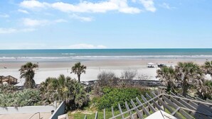 Vista a la playa con una terraza de madera y palmeras.