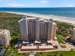 A high-rise hotel with multiple balconies, a parking lot, and a view of the beach and ocean. - Inlet at Minorca 1007 (New Smyrna Beach)