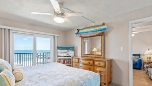 Une chambre dotée d’un grand lit, d’un ventilateur de plafond, d’une commode en bois, d’un miroir et offrant une vue sur l’océan grâce à une porte coulissante.