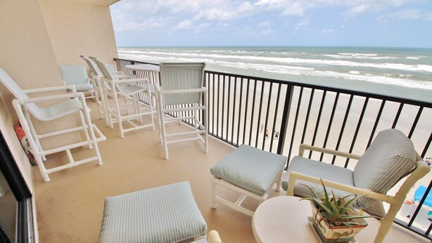 Un balcon avec des chaises blanches et une table, donnant sur l’océan.