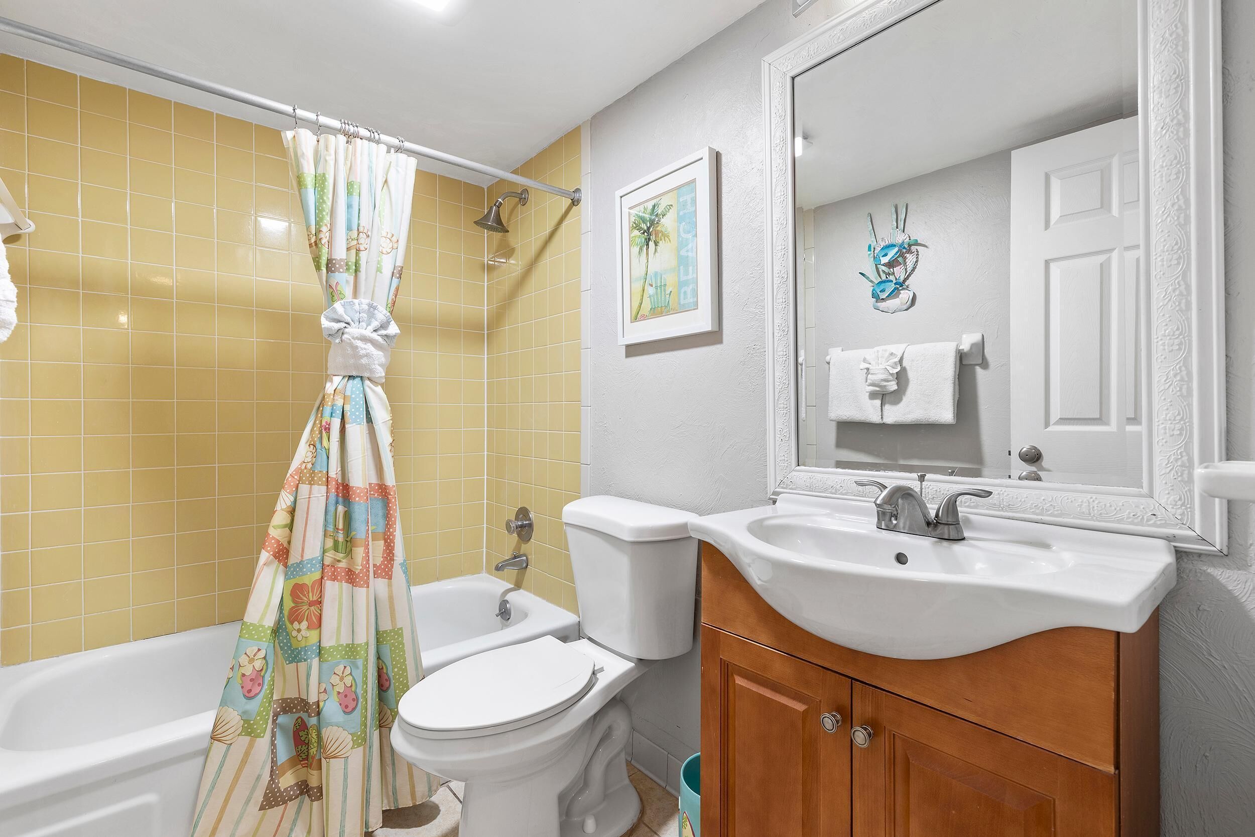 Een badkamer met gele tegels, een wit bad, een toilet en een wastafel met een houten kastje.