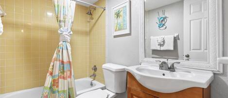 Een badkamer met gele tegels, een wit bad, een toilet en een wastafel met een houten kastje.