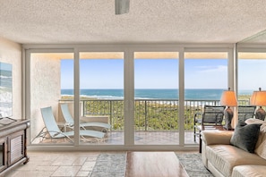 A room with a large sliding glass door leading to a balcony with a view of the ocean.