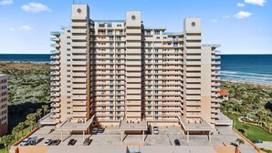 Un hôtel de grande hauteur doté de nombreux balcons, d’un parking et offrant une vue sur la plage.