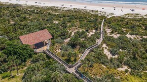 Vue aérienne d’un complexe hôtelier en bord de mer, avec une promenade en bois menant à un bâtiment doté d’un toit rouge.