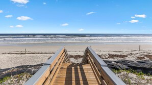 A wooden boardwalk leading to a beach with a clear blue sky and ocean.