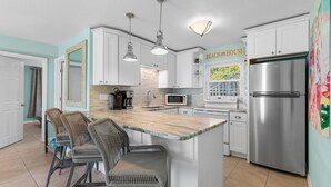 A kitchen with white cabinets, a stainless steel refrigerator, and a bar area with wicker chairs.
