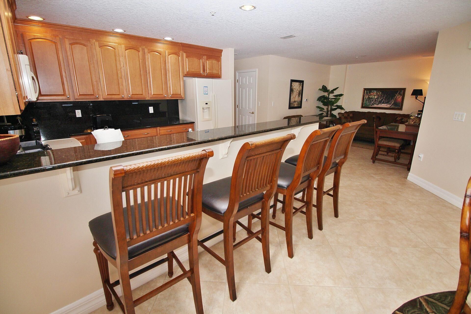 A kitchen with wooden cabinets, a black countertop, and a built-in bar with four wooden bar stools.