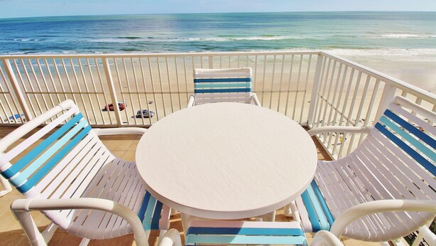 Een balkon aan het strand met een ronde tafel en gestreepte stoelen, met uitzicht op de oceaan.