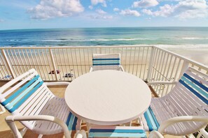 A beachside balcony with a round table and striped chairs, overlooking the ocean. - Malibu 704 (New Smyrna Beach)