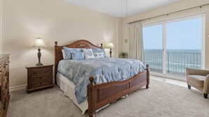 Een slaapkamer met een groot bed, twee nachtkastjes, een plafondventilator en uitzicht op de oceaan door een schuifdeur.