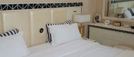 A hotel room with a bed, bedside table, lamp, mirror, and a wall-mounted air conditioning unit.