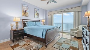A bedroom with a bed, nightstands, a chair, a ceiling fan, and a large window with a view. - Malibu 803 (New Smyrna Beach)