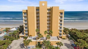 A multi-story hotel with a beach view, featuring balconies, a parking lot, and palm trees. - Malibu 803 (New Smyrna Beach)